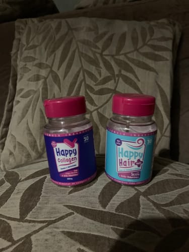 Cliente exibe um pote de Happy Hair e um pote de Happy Collagen sobre uma almofada.
