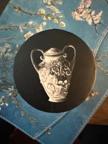 Customer's packaging for the Zodiac Pendant, showing the circular lid with a vase illustration on a floral surface.