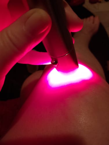 Vásárló használja a ClinicRed fototerápiás eszközt a térdén, ami erősen világít.