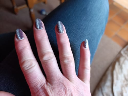 Kundin zeigt ihre fertige Maniküre mit dem glitzernden UV Gel Burgundy Cateye.