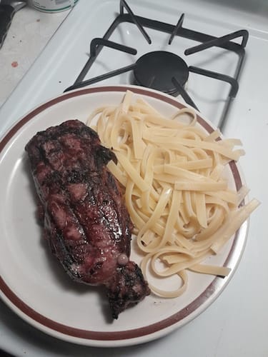 Reviewer's grilled New York Strip steak served on a plate with plain fettuccine pasta.
