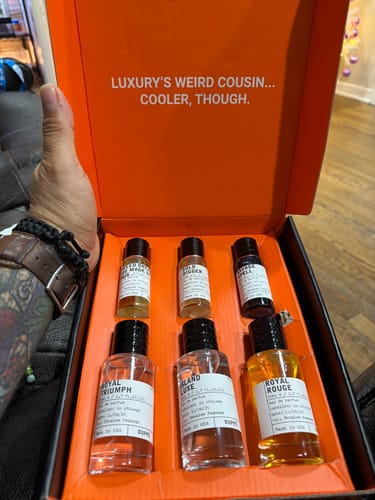 Customer holding an open orange box displaying a set of six assorted fragrance bottles.
