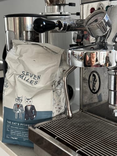 Customer's bag of The Cat's Pyjamas coffee sitting on a counter next to a chrome espresso machine.