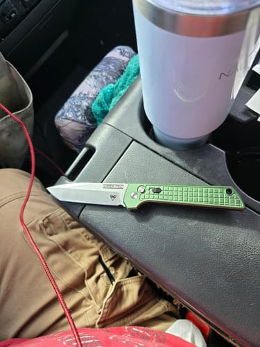 Reviewer's open VT Valiant D2 Switchblade with a green handle, shown resting on a car's center console.