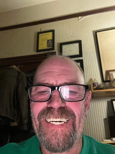 A close-up of a customer with glasses smiling broadly, showing a full set of bright white veneers.