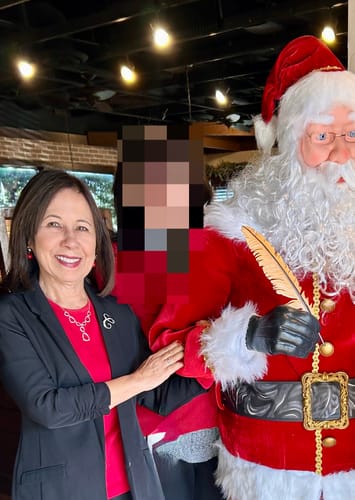 Customer wearing the red Hannah Long Sleeve Top layered under a jacket, standing next to a Santa Claus figure at a holiday event.