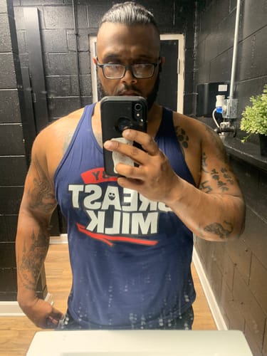 Reviewer taking a mirror selfie while wearing the blue Body By Breast Milk Tank Top in a dark bathroom.