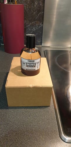 Il flacone del profumo CORIUM di un recensore, posato sulla sua scatola di cartone in una cucina.