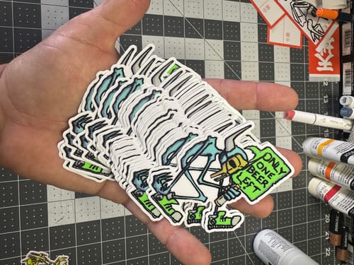 Customer holding a large stack of custom 3" vinyl stickers with a cartoon skeleton design.