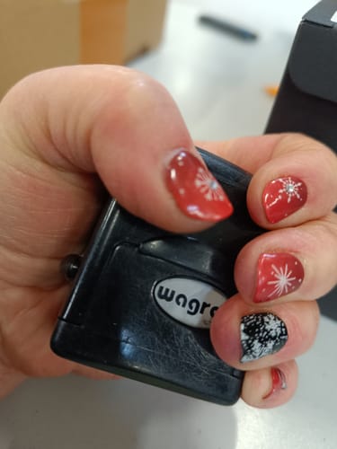 Eine Kundenhand zeigt eine Maniküre mit den roten 'Winter Rouge' UV-Gelfolien mit weißem Schneeflocken-Design.