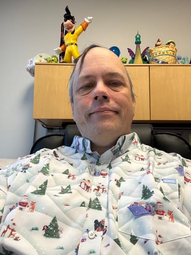 Reviewer in an office wearing the festive "Stop Motion Wonderland" KUNUFLEX long sleeve shirt, showing the detailed character pattern.