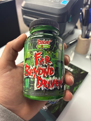 A reviewer holds up a green bottle of Far Beyond Driven dietary supplement capsules in their hand.