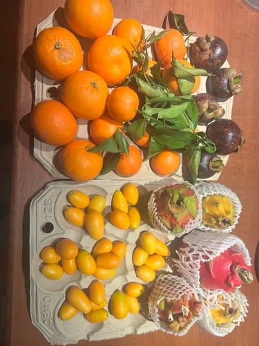 Kunde zeigt die bunte Obstvielfalt seiner Bestellung, darunter Mandarinen und Drachenfrüchte.