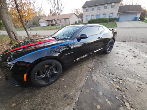 Customer's shiny black Camaro with red and blue stripes parked in a driveway, showing detailing results.