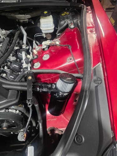Customer's black Motion Raceworks Catch Can Kit installed in the car's red engine bay.