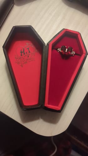 Customer's Promise Ring with a red heart-shaped stone, shown inside its open coffin-shaped box.