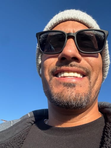 Customer smiling outdoors in sunglasses, showing a natural-looking smile with Pop On Veneers.