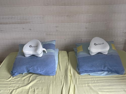 Photo d'un client montrant deux coussins orthopédiques pour genoux Cellsius, chacun posé sur un oreiller sur un lit.