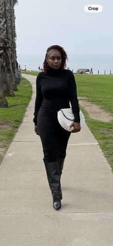 Customer walking outdoors, pairing the white Bahari Luxe Cowry Shell Clutch with a stylish black outfit.