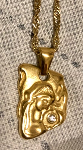 Close-up of a customer's gold Venus Pendant, showing the organic shape, a relief of a figure, and a small zirconia stone.