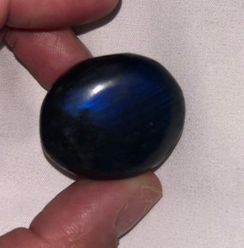 Close-up of a reviewer holding a dark Labradorite crystal showing a vibrant blue sheen.