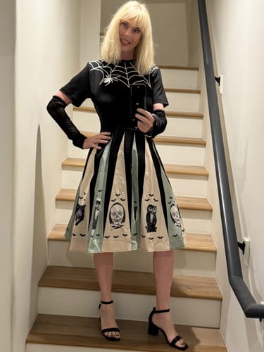 Customer wearing the 1950s Halloween dress with a spider web top and printed patchwork skirt on a staircase.