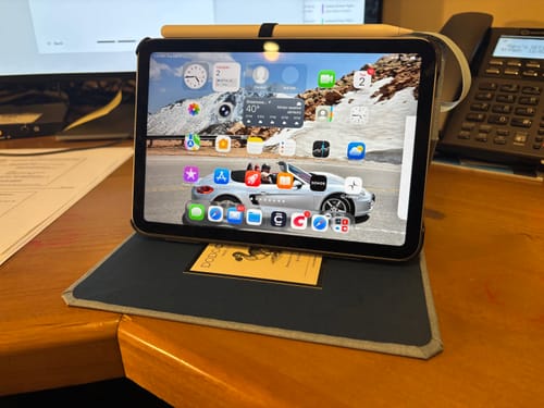 Reviewer's dark book-style iPad Mini case standing open on a desk, with a pencil held in the top loop.