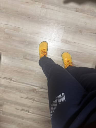 Partial view of a customer's feet in bright yellow shoes with orange laces on a wood floor.