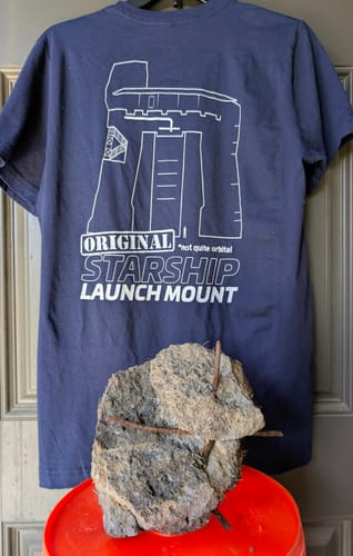 Customer's navy Original Launch Mount T-shirt shown with a piece of concrete from the launch mount.