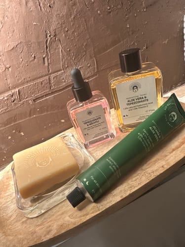Reviewer's Intensive Mask Routine products, including a soap bar, serum, tonic, and green tube, on a wooden surface.