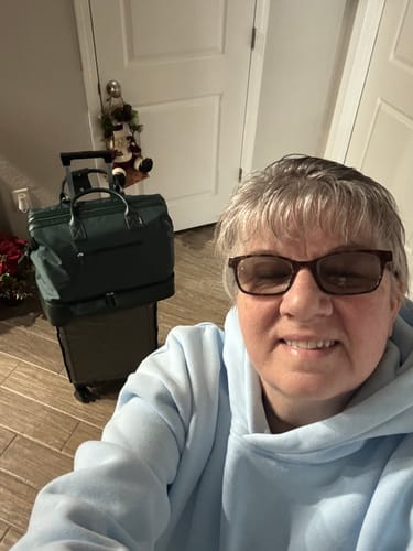 Customer taking a selfie with their green weekender bag stacked on a rolling carry-on suitcase.