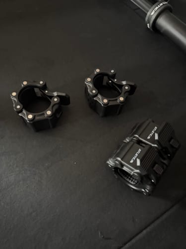 Ein Rezensent zeigt drei schwarze Pro Hantelverschlüsse auf einem dunklen Boden, die ihre magnetische Eigenschaft demonstrieren.