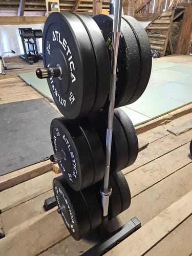 Kunde zeigt seine schwarzen 15-kg-Bumper-Plates, die auf einem Hantelständer gelagert sind.