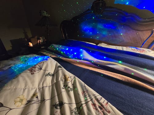 Customer's Wool Blanket in Pacific Nights layered on a bed under a blue and green galaxy light.