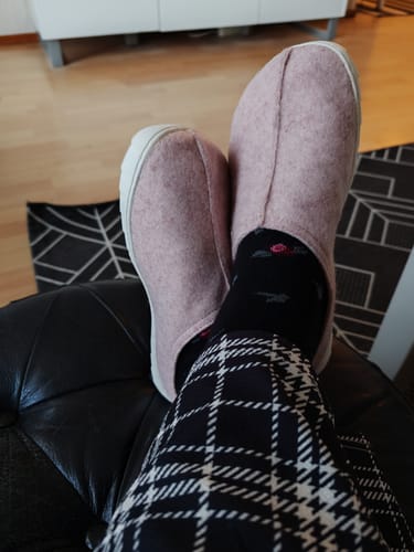 Asiakkaan jalassa vaaleanpunaiset Vaistoa Toive -paljasjalkatossut, jalat nostettuna lepäämään mustalle rahille.