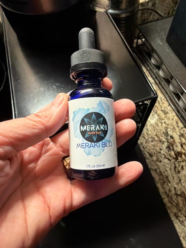 Reviewer holding the blue Meraki Blu Methylene Blue dropper bottle in their hand.