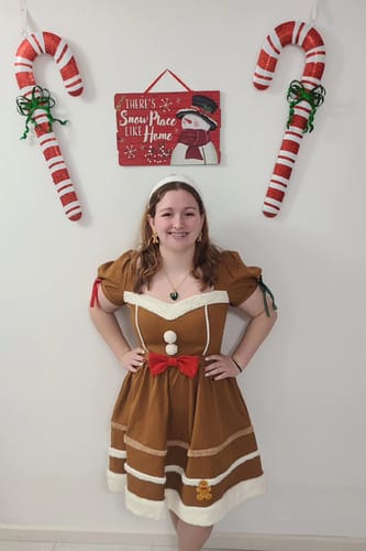 Reviewer posing in the brown gingerbread man dress, showing its red bow, puff sleeves, and white trim.