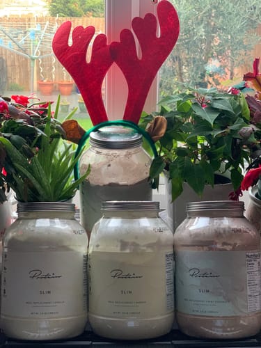 Customer's three large jars of Slim Meal Replacement powder on a windowsill, one with festive reindeer antlers.