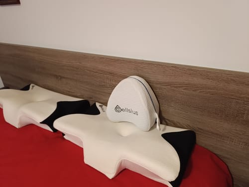 Photo d'un client montrant deux Coussins d'Alignement Cervical Cellsius sur un lit rouge.
