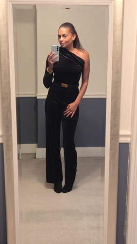 Customer taking a mirror selfie in the black Nightfall One Shoulder Velvet Jumpsuit, accessorized with a belt.