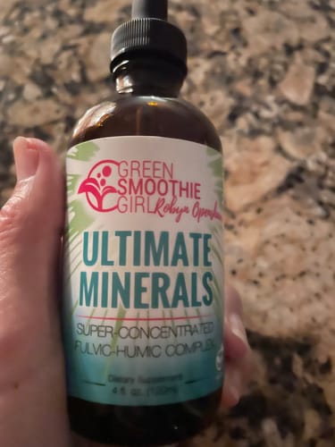 A reviewer holds up their brown glass bottle of Ultimate Minerals, showing the label and dropper top.