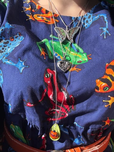 Reviewer wearing the closed silver Cosmic Heart Pendant layered with other necklaces against a colorful frog-print shirt.