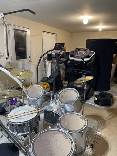 Reviewer's Sauna Pod 2.0 stored in a home gym filled with exercise equipment and a drum set.