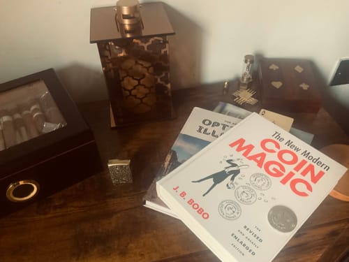 Customer's 'New Modern Coin Magic' book displayed on a wooden desk with a cigar box and other items.