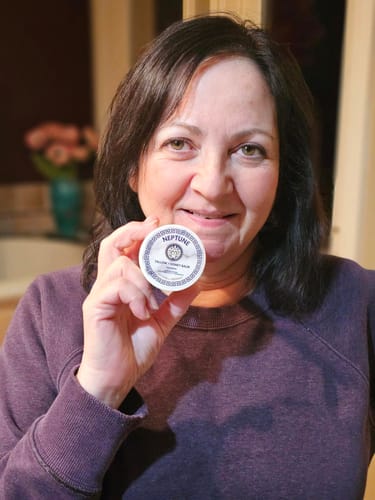 Reviewer smiling while holding up the round container of Grass Fed Tallow & Honey Balm.