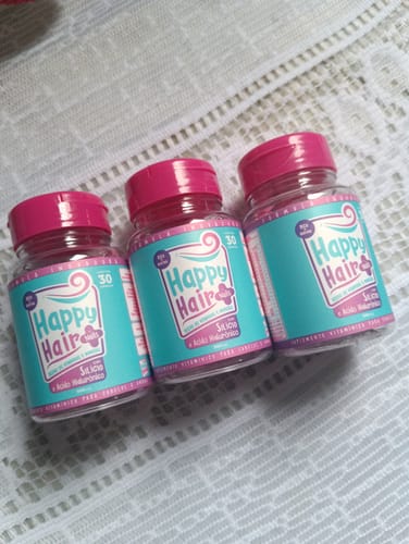 Cliente mostra os três potes do suplemento Happy Hair sobre uma toalha de renda branca.