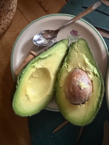 Kunde zeigt eine frische, aufgeschnittene Avocado aus dem Avocado-Mix auf einem Teller mit einem Löffel.