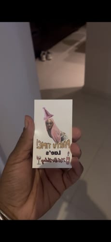 A reviewer holding a custom birthday tattoo before application. The design features a person in a pink party hat and mirrored text.