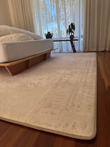 Reviewer's Mellow Mat in Sandstone Haze on a dark hardwood floor in a bright, modern bedroom.