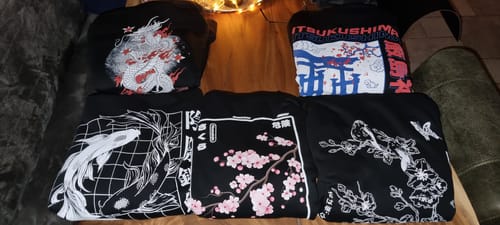 Reviewer's collection of five folded black Torii Gate hoodies with different detailed Japanese-inspired prints laid out on a table.